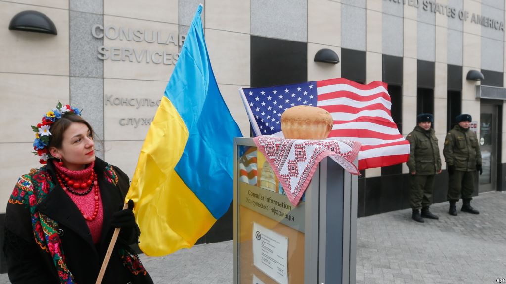 epa05734039 Ukrainian girl holds the National flag as shy stays close to traditional bread and salt, which they retain in front of the US embassy during their welcoming rally in Kiev, Ukraine, 20 January 2017, on the eve of President-elect Donald Trump's inauguration as the 45th president of the United States. Some Ukrainians gathered in front of the US embassy in Kiev to say goodbye to the former president Obama and welcome the new US president and hope on his support to stop the conflict in the eastern Ukraine and hold a peace in the world.  EPA/SERGEY DOLZHENKO