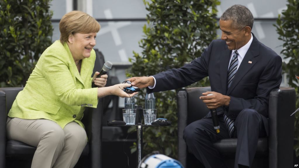 Former U.S. President Barack Obama, right, and German Chancellor Angela Merkel smile as Obama hands over a headphone for translation during a discussion event on democracy and global responsibility at a Protestant conference in Berlin, Germany, Thursday, May 25, 2017, when Germany marks the 500th anniversary of the Reformation. (AP Photo/Gero Breloer)