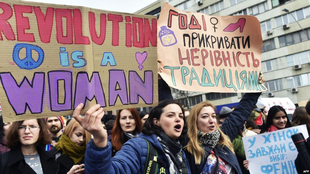 Ukrainian feminists hold placards reading "Revolution is a woman" and "Enough to cover inequality with traditions" during a march on March 8, 2017 in Kiev, as part of International Women's Day. / AFP PHOTO / Sergei SUPINSKY